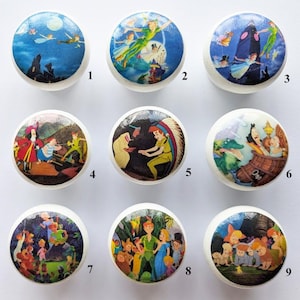 May include: Nine white wooden cabinet knobs featuring scenes from the animated film Peter Pan. The knobs depict Peter Pan, Captain Hook, Tinkerbell, and other characters. Each round knob has a glossy finish and is suitable for furniture.