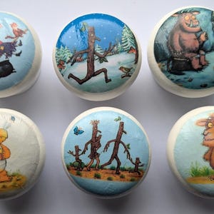 May include: Six round wooden knobs with colourful illustrations from the children's book, 'Where the Wild Things Are'. The knobs feature a witch on a broomstick, a stick man running, a monster sitting on a log, a dragon, a family of stick people, and a monster standing.