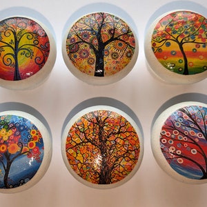 May include: Six round white ceramic knobs with colourful tree designs. Each knob features a different tree design with various colours, including red, orange, yellow, green, blue, and purple.