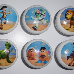 May include: Six round white ceramic knobs featuring colourful images of characters from the Toy Story movie franchise. The characters include Woody, Buzz Lightyear, Slinky Dog, Rex, Mr. and Mrs. Potato Head, and Bullseye.