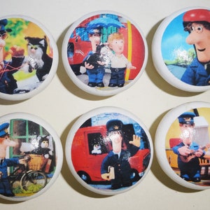 May include: Six round ceramic knobs featuring colourful images of a cartoon postman character. The postman is wearing a blue uniform and a red hat. The images include the postman delivering mail, riding a bicycle, and playing a guitar.