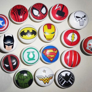 May include: A set of 16 round, white ceramic drawer knobs featuring colourful superhero and comic book character designs. The designs include Superman, Batman, Spiderman, Iron Man, The Flash, Deadpool, The Hulk, Captain America, Wonder Woman, Thor, Green Lantern, and more.