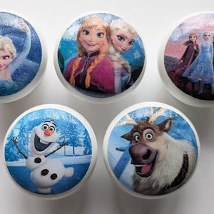 May include: Set of five round ceramic drawer knobs featuring characters from the animated film Frozen. The knobs feature Elsa, Anna, Olaf, Sven the reindeer, and Kristoff.
