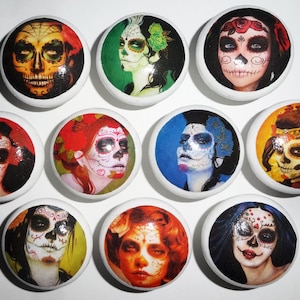 May include: A set of ten round white ceramic cabinet knobs, each featuring a unique, colourful portrait of a person with detailed sugar skull face paint. The designs include various floral accents, vibrant hair colours, and intricate decorative patterns.
