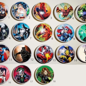 May include: Set of 18 round ceramic cabinet knobs featuring various superhero and comic book characters. The knobs are white with colourful images of characters like Superman, Batman, Spiderman, Wolverine, and more.