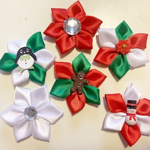 Peut inclure: Six décorations de Noël en forme de fleurs faites à la main. Chaque fleur est faite de ruban de satin rouge, blanc et vert. Certaines ont des centres en strass, tandis que d'autres présentent un pingouin, un bonhomme en pain d'épices ou un bonhomme de neige.