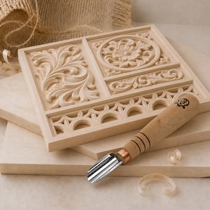 May include: A light-colored wooden panel featuring intricate carved floral and geometric patterns, including a circular medallion and scrolling leaves. A wood carving gouge with a metal blade and a wooden handle rests on the panel.