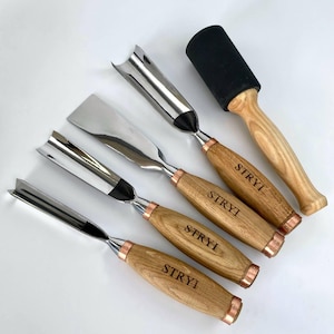 May include: A set of four metal wood carving chisels with light brown wooden handles branded with the text STRYI and a wooden mallet with a black rubber head. Each chisel features a polished steel blade and a copper-coloured metal ferrule.