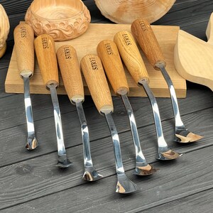 Peut inclure: Un ensemble de sept outils de sculpture sur bois avec des lames en m&eacute;tal poli et des manches en bois brun clair. Chaque manche porte l'inscription STRYI. Les outils pr&eacute;sentent des pointes m&eacute;talliques incurv&eacute;es en forme de cuill&egrave;re.