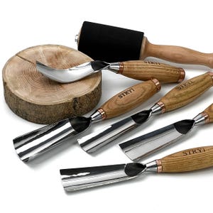 May include: A collection of wood carving tools, including gouges, a spoon carving knife, and a roller. The tools have wooden handles with metal blades and accents. A wooden slice is also included.