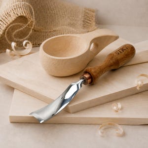 May include: A light-colored wooden kuksa cup with a side handle and a metal wood carving gouge featuring a dark wooden handle engraved with the text STRY. The gouge has a curved, polished steel blade and a copper-colored metal ferrule.
