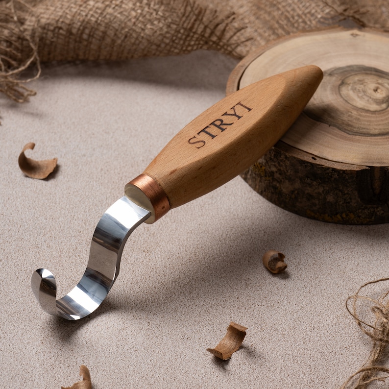May include: A wooden carving tool with a curved blade and a wooden handle. The handle is engraved with the word "STRYI".