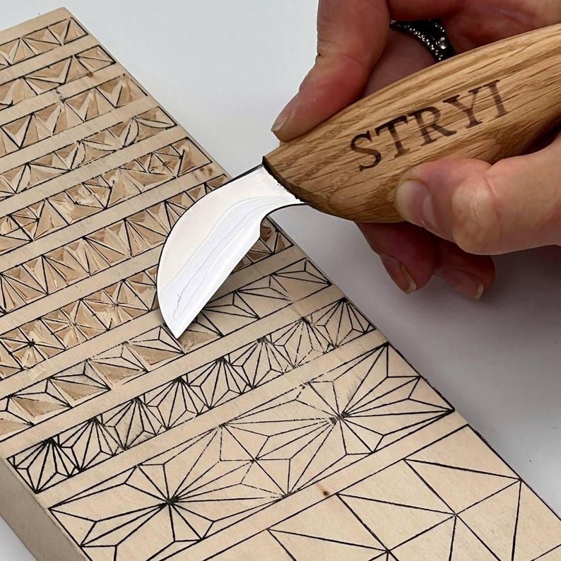 May include: A wood carving knife with a curved blade is held over a wooden block with geometric patterns. The knife handle is engraved with the word "STRYI". The wooden block features various carved designs, including triangles and starburst shapes.