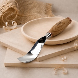 May include: A metal spoon gouge with a curved, polished steel blade and a light brown wooden handle featuring the brand name STRYI engraved on the side. The tool has a copper-colored metal ferrule connecting the blade to the handle.