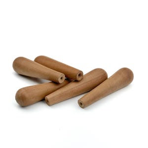 May include: A collection of five light brown wooden handles, each featuring a tapered, cylindrical shape with a rounded end and a small, centered circular hole at the narrower base, showcasing a smooth, natural wood grain texture throughout.