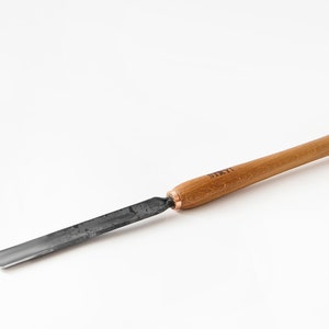 Puede incluir: Una herramienta de talla de madera con una cuchilla de metal negro y un mango de madera. El mango está etiquetado con "STRYT" en letras negras.