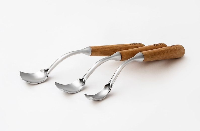 以下が含まれることがあります： 曲がったステンレス鋼の刃と木製の柄が付いた、3つの彫刻刀。柄は明るい茶色で円筒形で、それぞれに「SIKTI」の文字が刻まれています。刃は湾曲した形状で、白い背景に配置されています。