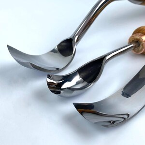 May include: Three curved metal carving tools with wooden handles. The tools are arranged in a row, with the largest tool at the bottom and the smallest tool at the top. The tools are all shiny and have a reflective surface.
