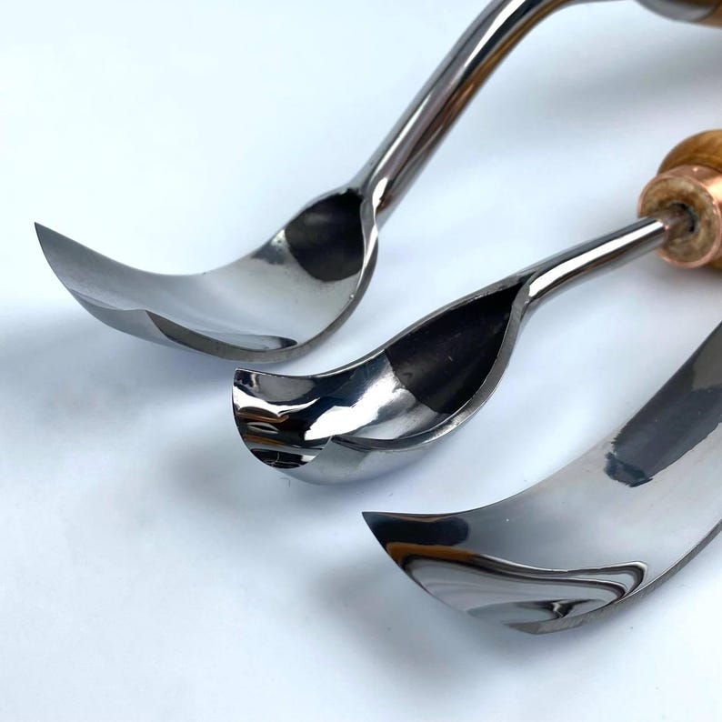 May include: Three curved metal carving tools with wooden handles. The tools are arranged in a row, with the largest tool at the bottom and the smallest tool at the top. The tools are all shiny and have a reflective surface.