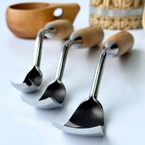 May include: Three carving tools with wooden handles and curved metal blades. The tools are arranged in a row on a white surface.