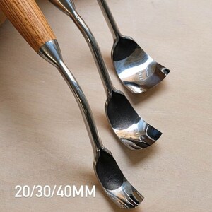 以下が含まれることがあります： 木製の柄が付いた金属製の彫刻刀が3本。彫刻刀は湾曲した刃を持ち、斜めに配置されています。「20/30/40MM」の文字が下にあります。これらのツールは、木工や彫刻用に設計されています。