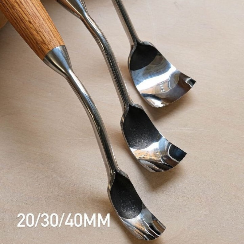 以下が含まれることがあります： 木製の柄が付いた金属製の彫刻刀が3本。彫刻刀は湾曲した刃を持ち、斜めに配置されています。「20/30/40MM」の文字が下にあります。これらのツールは、木工や彫刻用に設計されています。