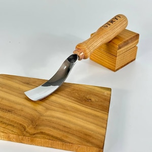 May include: A wood carving tool with a curved blade and a wooden handle. The handle is engraved with the word "LRYI".