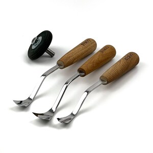 May include: Three wood carving tools with curved metal blades and light brown wooden handles, each stamped with the brand name STRYI, accompanied by a small black circular rubber wheel with a central metal bolt and a short metal shaft.