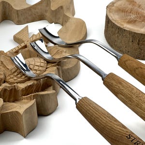 May include: Three wood carving tools with curved, polished metal blades and light brown wooden handles. The tools feature distinctively shaped, sharp metal tips designed for gouging and shaping wood, with the brand name STR visible.