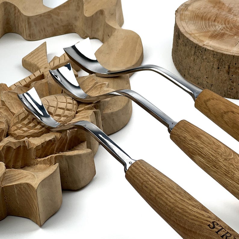 May include: Three wood carving tools with curved, polished metal blades and light brown wooden handles. The tools feature distinctively shaped, sharp metal tips designed for gouging and shaping wood, with the brand name STR visible.