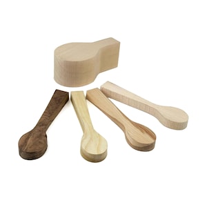 May include: A collection of five unfinished wooden spoon blanks in various wood tones, including light beige, medium tan, and dark brown. The set features four elongated spoon shapes with flat handles and one thicker, rounded block-shaped piece.