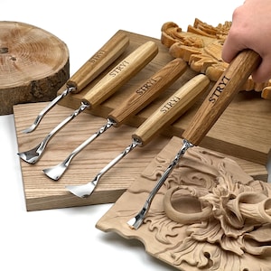 May include: A set of five wood carving tools with light brown wooden handles, each branded with the text STRYI. The tools feature silver-colored metal shafts with a twisted design and curved, sharp blades for detailed woodworking tasks.
