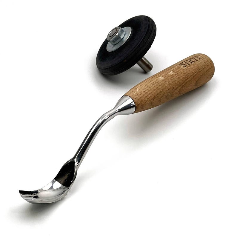 May include: A wood-handled carving tool with a curved, polished metal scoop and a separate black rubber wheel attachment. The wooden handle features the brand name STRYI engraved on the surface. The tool has a metallic neck connecting the handle.