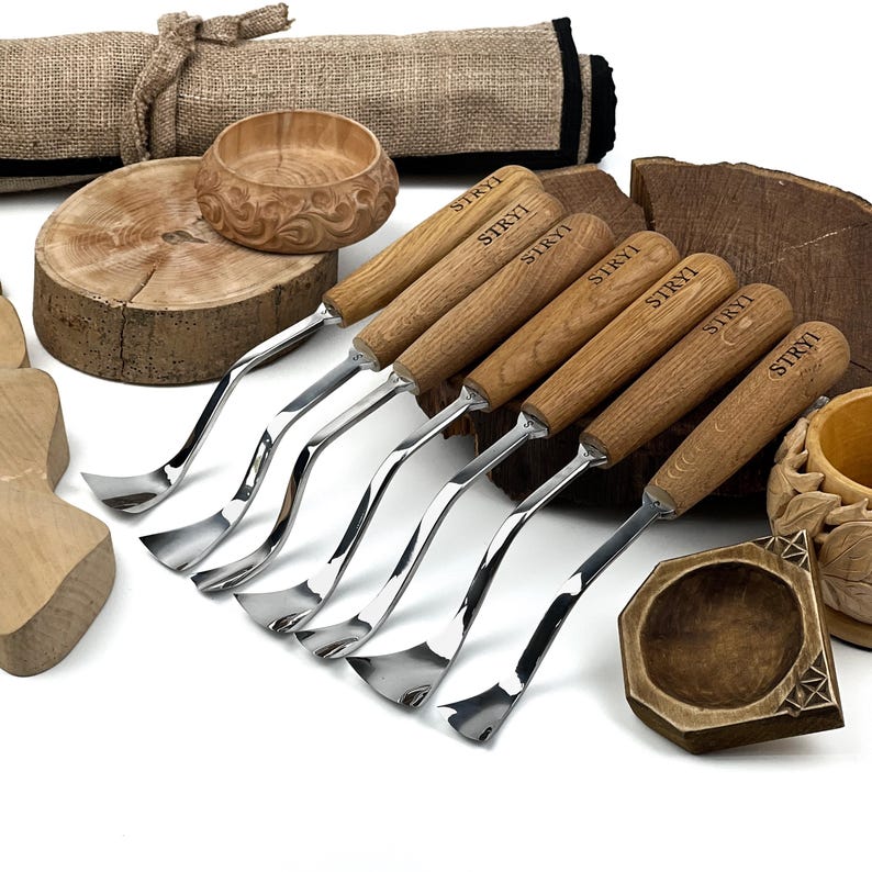 Peut inclure: Un ensemble de six outils de sculpture sur bois en m&eacute;tal avec des manches en bois brun clair, chacun marqu&eacute; du texte STRYI. Les outils pr&eacute;sentent des lames m&eacute;talliques polies et incurv&eacute;es, dispos&eacute;s avec des bols et blocs en bois.