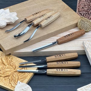 Puede incluir: Un juego de seis herramientas para tallar madera con mangos de madera marrón claro, cada una marcada con el texto STRYI. Tres herramientas cuentan con hojas de metal curvas, mientras que tres tienen hojas de metal rectas.