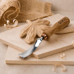 May include: A wood carving gouge with a curved, polished metal blade and a light brown wooden handle featuring the brand name STRYI burned into the wood. The tool has a copper-coloured metal ferrule connecting the blade to the handle.