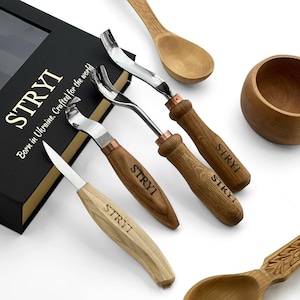 May include: A collection of wood carving tools with stainless steel blades and wooden handles. The handles are engraved with "STRYI". The tools are arranged near a black box with gold lettering that reads "STRYI Born in Ukraine. Crafted for the world."
