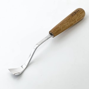 May include: A wood carving gouge with a curved, polished steel blade and a wooden handle. The handle is light brown with the word "STRYI" etched into the wood. The blade curves to a rounded, scoop-like shape.