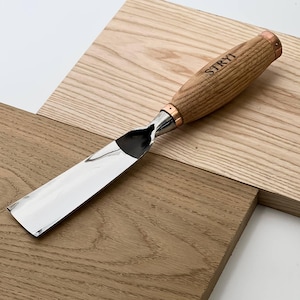 May include: A wood carving chisel with a polished, flat metal blade and a light brown wooden handle. The handle features a copper-colored metal ferrule and the brand name STRYI is clearly engraved in black lettering on the side of the wood.