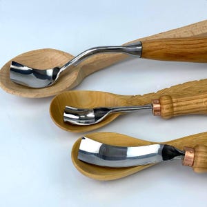 May include: Three wooden spoons with metal carving tools attached to the handles. The tools are different shapes and sizes. The spoons are made of light wood.