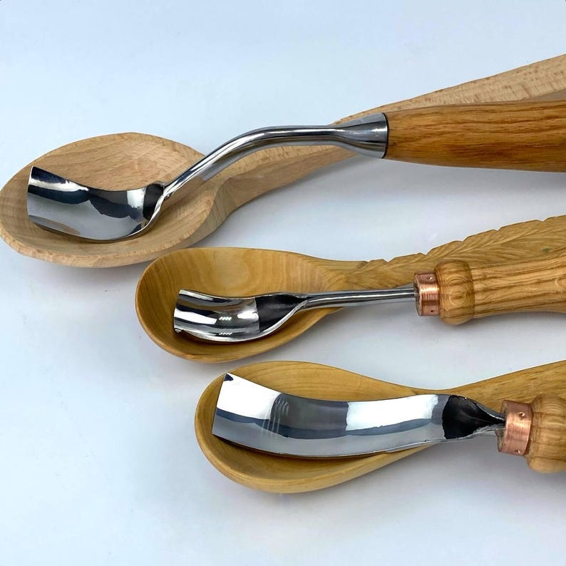May include: Three wooden spoons with metal carving tools attached to the handles. The tools are different shapes and sizes. The spoons are made of light wood.