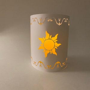 May include: White paper lantern with a cut-out design of a sun with rays. The lantern has a decorative border around the top and bottom.
