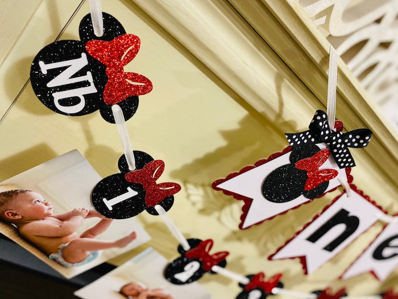 May include: Black and red Minnie Mouse themed photo banner with the word "one" and numbers 1, 2, 3, and 4. The banner is strung with white ribbon and has black and white polka dot bows.