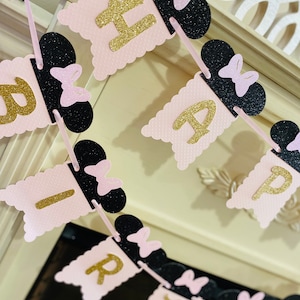 May include: Pink and black banner with gold glitter letters spelling "Happy Birthday". Each letter is attached to a black Mickey Mouse ear with a pink bow.