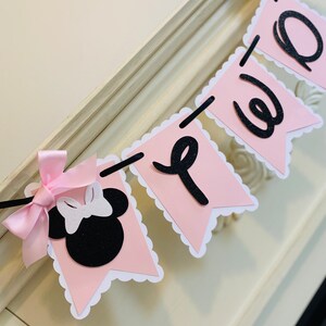 May include: Pink and black banner with the word "Welcome" in black letters. The banner has a scalloped edge and features a black and white Minnie Mouse head with a pink bow.