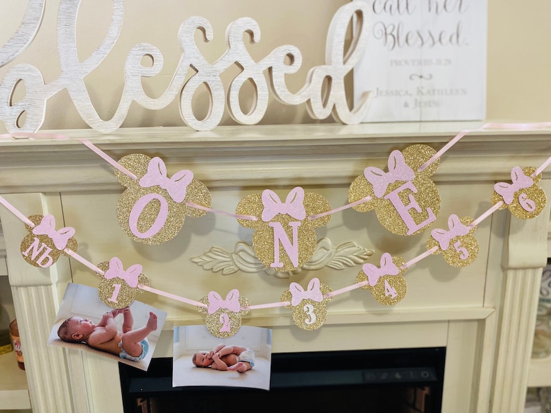 May include: A pink and gold glitter banner with Mickey Mouse ears and numbers from 0 to 6. The banner says "Blessed" and has a pink ribbon.