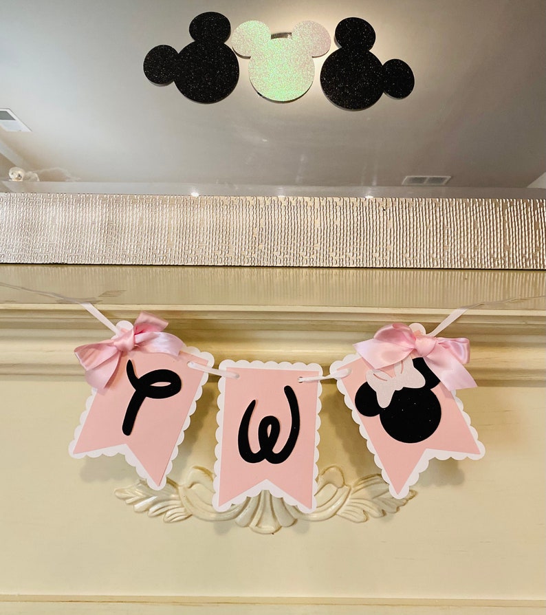 May include: Pink and black banner with the letters "PW" and a black silhouette of Minnie Mouse with a pink bow. The banner is strung with pink ribbon.
