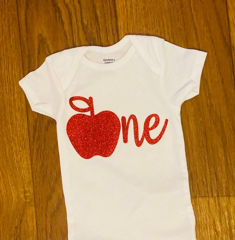 May include: White onesie with a red glitter apple and the word "one" in red glitter.