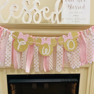 May include: A decorative banner with gold glitter Mickey Mouse head cutouts spelling "TWO". The banner is adorned with pink bows and ribbons, and is set against a backdrop of pink and gold polka dot fabric. A sign reads "Children rise up and call her Blessed."