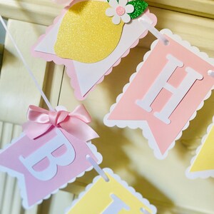 May include: A pink and yellow banner with the words "Happy Birthday" in white letters. The banner is decorated with pink bows, a lemon slice, and green leaves.